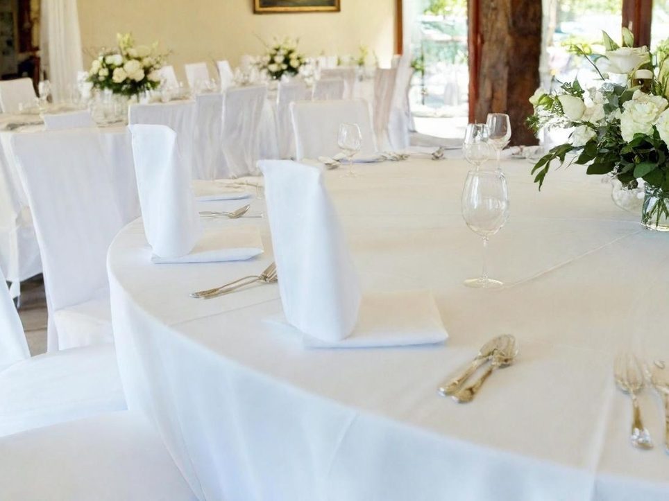 Leihwäsche für Hochzeiten, Firmenfeiern, Events Ein elegant gedeckter Tisch mit weißen Tischdecken und Blumenarrangements.